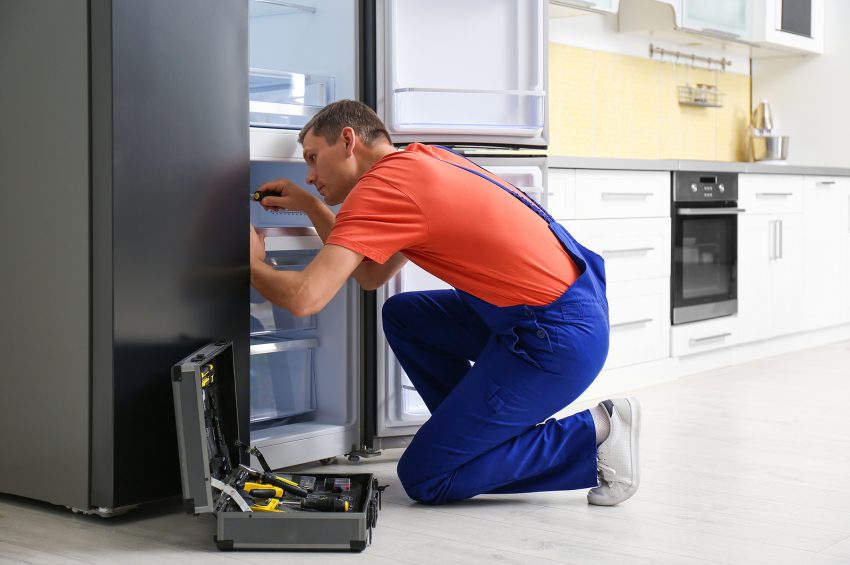 Male Technician With Screwdriver Repairing Refrigerator In Kitch
